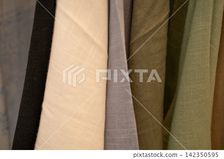 Close up of neutral fabric swatches hanging in fashion studio. Natural textile texture. Sustainable clothing design, ethical sourcing and conscious material selection. Sustainable fashion materials. Close up of neutral fabric swatches hanging in fashion studio. Natural textile texture. Sustainable clothing design, ethical sourcing and conscious material selection. Sustainable fashion materials. 142350595