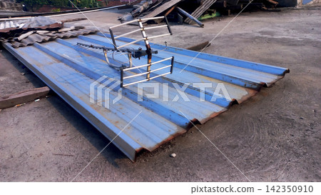 A disused outdoor TV antenna lay on a sheet of worn, blue corrugated metal. A disused outdoor TV antenna lay on a sheet of worn, blue corrugated metal. 142350910
