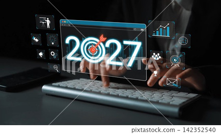 A business professional interacts with a digital interface showcasing trends and goals for 2027, emphasizing innovation and strategic planning in a modern workspace. Sigmoid A business professional interacts with a digital interface showcasing trends and goals for 2027, emphasizing innovation and strategic planning in a modern workspace. Sigmoid 142352540