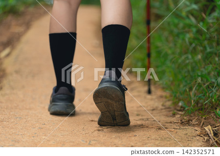 Close-up of woman leg walking on dirt trail wearing black socks and athletic shoes with hiking stick support in nature 142352571