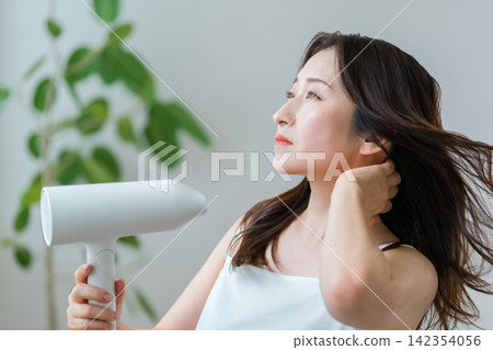 A woman in her 40s drying her hair with a hairdryer: hair care and hair care habits. A woman in her 40s drying her hair with a hairdryer: hair care and hair care habits. 142354056