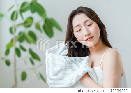 A woman in her 40s towel-dries her hair after washing it; hair care routine. A woman in her 40s towel-dries her hair after washing it; hair care routine. 142354311