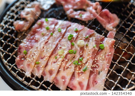 Fresh sliced pork belly grilling hot barbecue topped sesame seeds green onion for savory Korean style dining experience 142354340