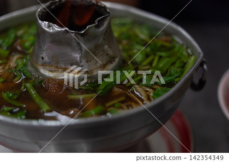 Traditional Thai hot pot tender beef assorted offal simmering rich savory broth fresh green vegetables served metal chimney pot Traditional Thai hot pot tender beef assorted offal simmering rich savory broth fresh green vegetables served metal chimney pot 142354349