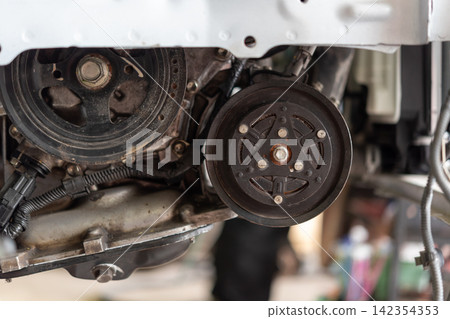 Closeup of automotive engine pulley compressor components showing mechanical parts wiring metal assembly during vehicle maintenance repair Closeup of automotive engine pulley compressor components showing mechanical parts wiring metal assembly during vehicle maintenance repair 142354353
