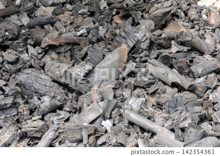 Pile of burned hardwood charcoal pieces showing black gray textures irregular shapes suitable for fuel barbecue cooking traditional charcoal production Pile of burned hardwood charcoal pieces showing black gray textures irregular shapes suitable for fuel barbecue cooking traditional charcoal production 142354361