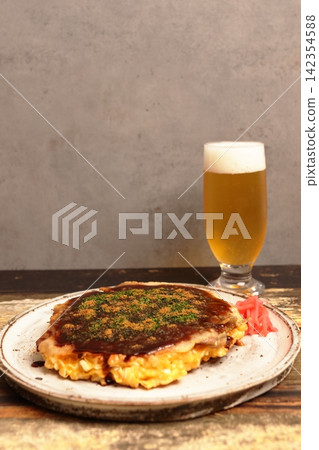 Freshly made okonomiyaki and a cold beer with a wall as the backdrop. 142354588