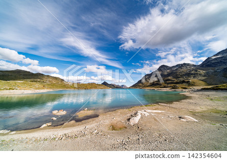 Scenic Alpine Mountain Lake with Clear Water and Rocky Shore under Blue Sky Scenic Alpine Mountain Lake with Clear Water and Rocky Shore under Blue Sky 142354604