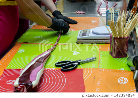 Confectioner Measuring Striped Candy String Next to Wooden Sticks and Scissors Confectioner Measuring Striped Candy String Next to Wooden Sticks and Scissors 142354854