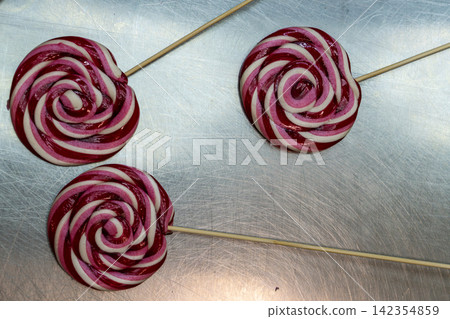 Three Round Swirl Lollipops with Wooden Sticks on Stainless Steel Counter Top 142354859
