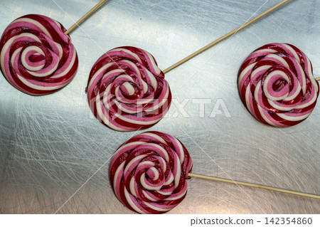 Four Swirl Lollipops with Long Wooden Skewers on Scratched Metal Surface Four Swirl Lollipops with Long Wooden Skewers on Scratched Metal Surface 142354860