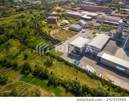 Drone view of industrial plant building with railway line next to green fields Drone view of industrial plant building with railway line next to green fields 142354909