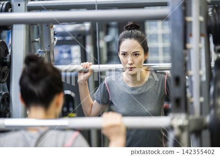 一位年輕女子正在鍛煉,她的身影映在鏡子裡。 一位年輕女子正在鍛煉,她的身影映在鏡子裡。 142355402