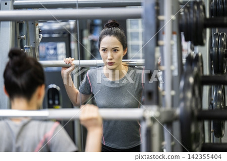 一位年輕女子正在鍛煉,她的身影映在鏡子裡。 一位年輕女子正在鍛煉,她的身影映在鏡子裡。 142355404