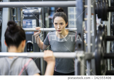 A young woman exercising, reflected in a mirror. A young woman exercising, reflected in a mirror. 142355406