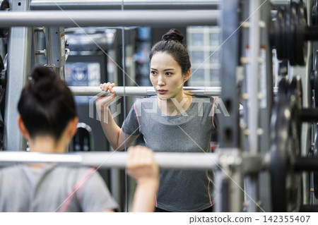 一位年輕女子正在鍛煉,她的身影映在鏡子裡。 一位年輕女子正在鍛煉,她的身影映在鏡子裡。 142355407