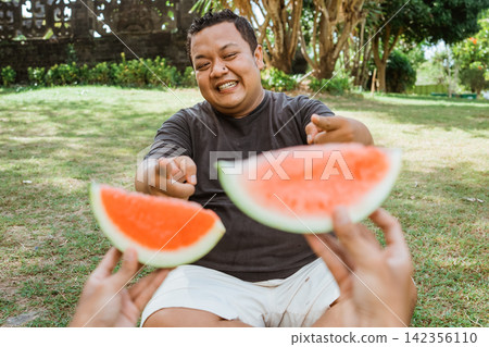 fat man with accepting gesture when offered watermelon in outdoor background 142356110