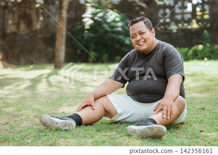 Asian fat man smiling in sportswear sitting down in an outdoor background Asian fat man smiling in sportswear sitting down in an outdoor background 142356161