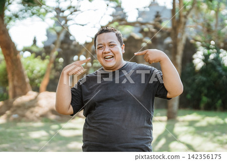 smiling Fat Man Standing with two hands pointing to his smile smiling Fat Man Standing with two hands pointing to his smile 142356175