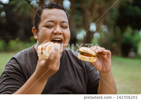 fat asian man holding bread and opening mouth while eating 142356201