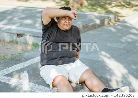 fat Asian man resting while wiping sweat from his face after jogging fat Asian man resting while wiping sweat from his face after jogging 142356202