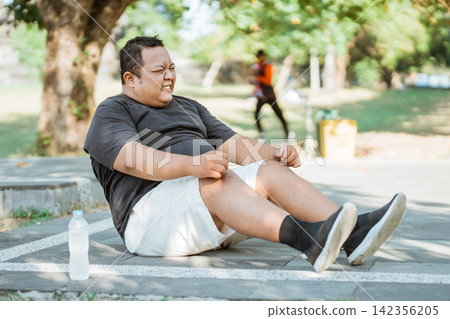 overweight man struggles to do a situp while exercising in the park overweight man struggles to do a situp while exercising in the park 142356205
