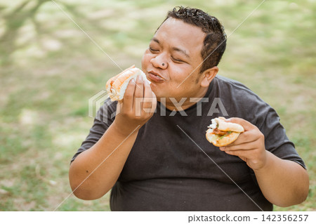 fat man happily eating bread while two hands hold bread fat man happily eating bread while two hands hold bread 142356257