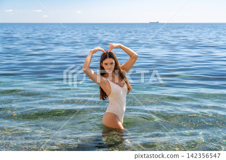 Woman beach heart Young woman in a white swimsuit makes a heart shape with her hands while standing in the clear ocean water Woman beach heart Young woman in a white swimsuit makes a heart shape with her hands while standing in the clear ocean water 142356547