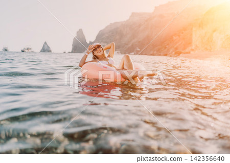 Woman, floating, sea. Young woman enjoying summer vacation, relaxing on inflatable ring near rocky coast. Woman, floating, sea. Young woman enjoying summer vacation, relaxing on inflatable ring near rocky coast. 142356640