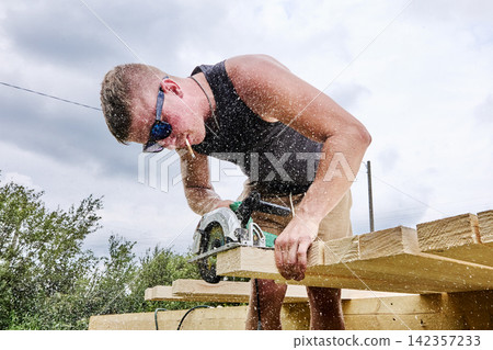 Circular saw cuts timber board for wood frame house construction, worker trims lumber during structural framing. Circular saw cuts timber board for wood frame house construction, worker trims lumber during structural framing. 142357233