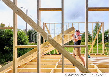 Timber frame construction, worker manually raising a prefabricated timber wall frame into an upright position. 142357235