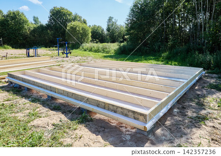Timber floor frame assembled on concrete blocks with parallel wooden joists forming base for future building construction. Timber floor frame assembled on concrete blocks with parallel wooden joists forming base for future building construction. 142357236