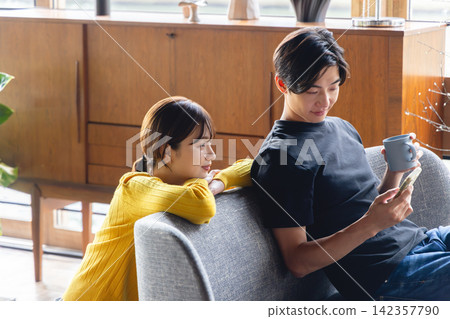 一對夫婦在客廳裡一邊看手機一邊聊天。 142357790