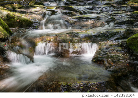 A waterfall leading to the Kikuchi Gorge with a clear stream flowing through nature A waterfall leading to the Kikuchi Gorge with a clear stream flowing through nature 142358104
