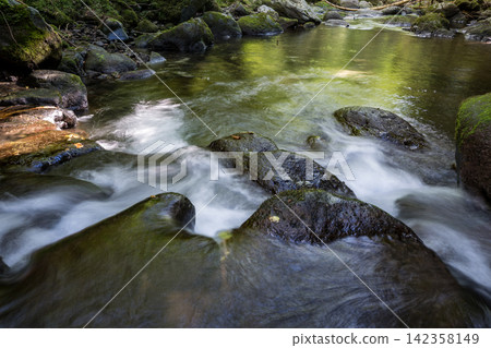 A waterfall leading to the Kikuchi Gorge with a clear stream flowing through nature A waterfall leading to the Kikuchi Gorge with a clear stream flowing through nature 142358149