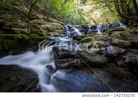 A waterfall leading to the Kikuchi Gorge with a clear stream flowing through nature A waterfall leading to the Kikuchi Gorge with a clear stream flowing through nature 142358150