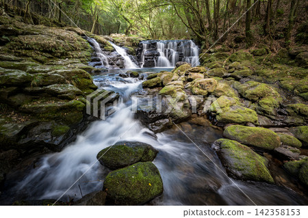 A waterfall leading to the Kikuchi Gorge with a clear stream flowing through nature A waterfall leading to the Kikuchi Gorge with a clear stream flowing through nature 142358153