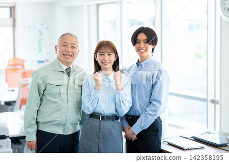 A man in work clothes and a young employee are seen smiling and making a victory pose in the office. A man in work clothes and a young employee are seen smiling and making a victory pose in the office. 142358195