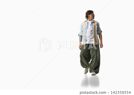 Fashionable man stands in striped top and loose green pants on white Fashionable man stands in striped top and loose green pants on white 142358554