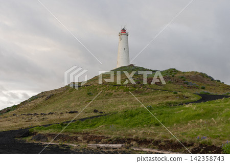 Reykjanes Lighthouse above a winding path on a grassy volcanic hill, Iceland 142358743