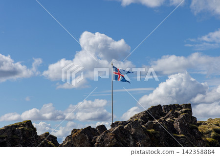Icelandic flag waving beneath large summer clouds, Thingvellir National Park, Iceland Icelandic flag waving beneath large summer clouds, Thingvellir National Park, Iceland 142358884