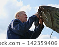 Car body shop. Repair man processes the welding seam using an angle grinder on replaced car part. Professional Body master grind old paint and rust. Rust damage. Rusting car. Hands with tool close-up 142359406