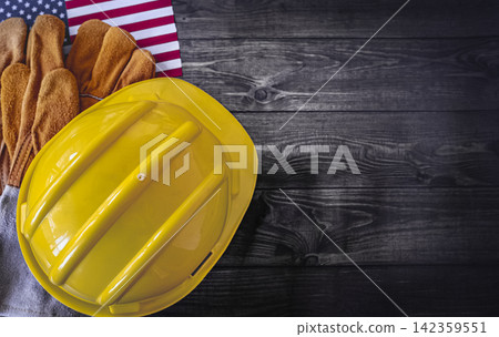Labor Day Concept with the flag of America hard hat and workwear gloves on dark wooden background Labor Day Concept with the flag of America hard hat and workwear gloves on dark wooden background 142359551