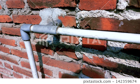 Horizontal PVC water pipe on a rough red brick wall. Horizontal PVC water pipe on a rough red brick wall. 142359674