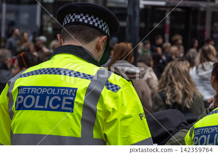 British police officer in high-visibility jacket standing near a public crowd British police officer in high-visibility jacket standing near a public crowd 142359764