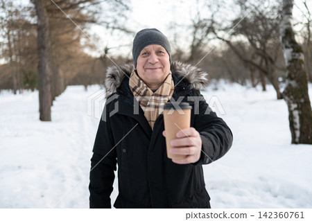 Smiling senior man offering hot coffee during winter walk 142360761