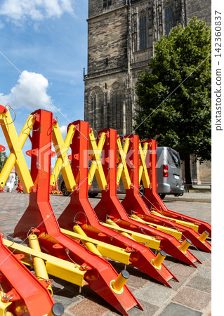 Portable red and yellow security barriers stand on cobblestone square beside historic Gothic church. Heavy mobile roadblocks provide temporary vehicle access control during event in Magdeburg Portable red and yellow security barriers stand on cobblestone square beside historic Gothic church. Heavy mobile roadblocks provide temporary vehicle access control during event in Magdeburg 142360837