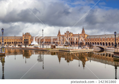 View of Plaza de Espana in Seville Spain with towers and canal. Renaissance Revival architecture under cloudy overcast sky View of Plaza de Espana in Seville Spain with towers and canal. Renaissance Revival architecture under cloudy overcast sky 142361860