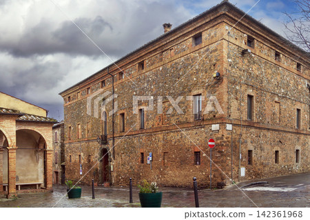 Historic brick building in Montalcino Italy opposite Sant Agostino church. Medieval architecture during rainy overcast day Historic brick building in Montalcino Italy opposite Sant Agostino church. Medieval architecture during rainy overcast day 142361968