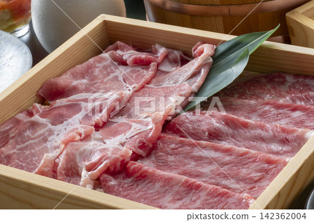 Thinly sliced beef served in a wooden shabu-shabu pot, garnished with green onions, creates a beautiful Japanese dining experience. 142362004